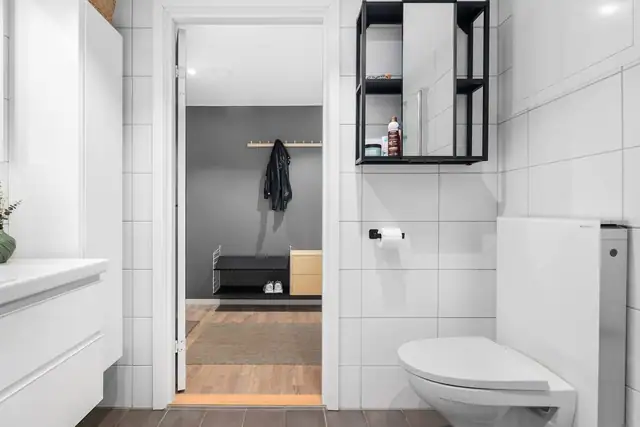 Badet er utstyrt med dusjhjørne, opplegg for vaskemaskin, vegghengt toalett og moderne baderomsinnredning.