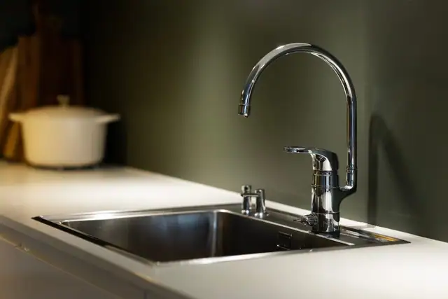 Detaljbilde av kjøkkenets stilrene benkeplate, romslige stålvask og elegante blandebatteri.