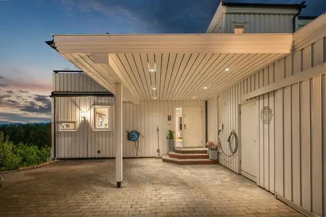 Pent inngangsparti med carport med takbelysning. Det er montert elbil-lader i carporten. Inngang til 2 uteboder her.